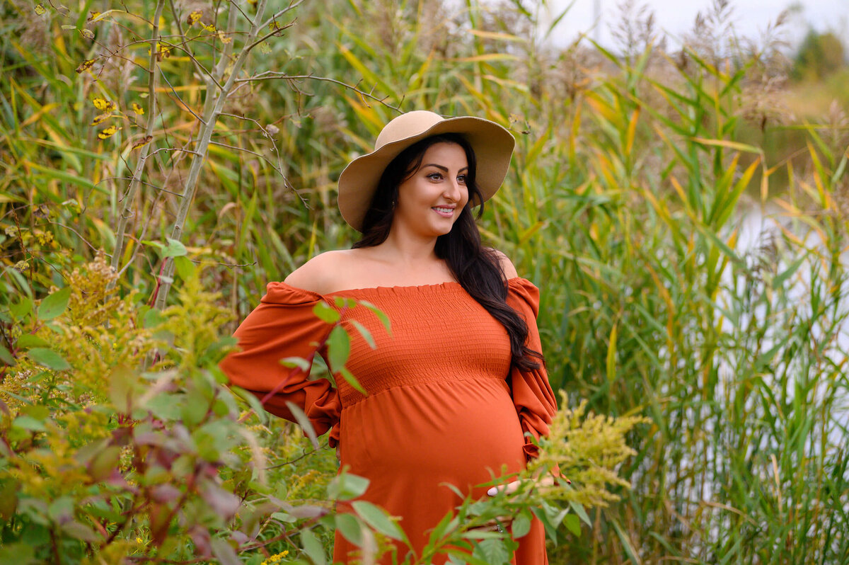 pregnant woman wearing an orange maternity dress with a beige hat for her Burlington, ON outdoor fall maternity photos