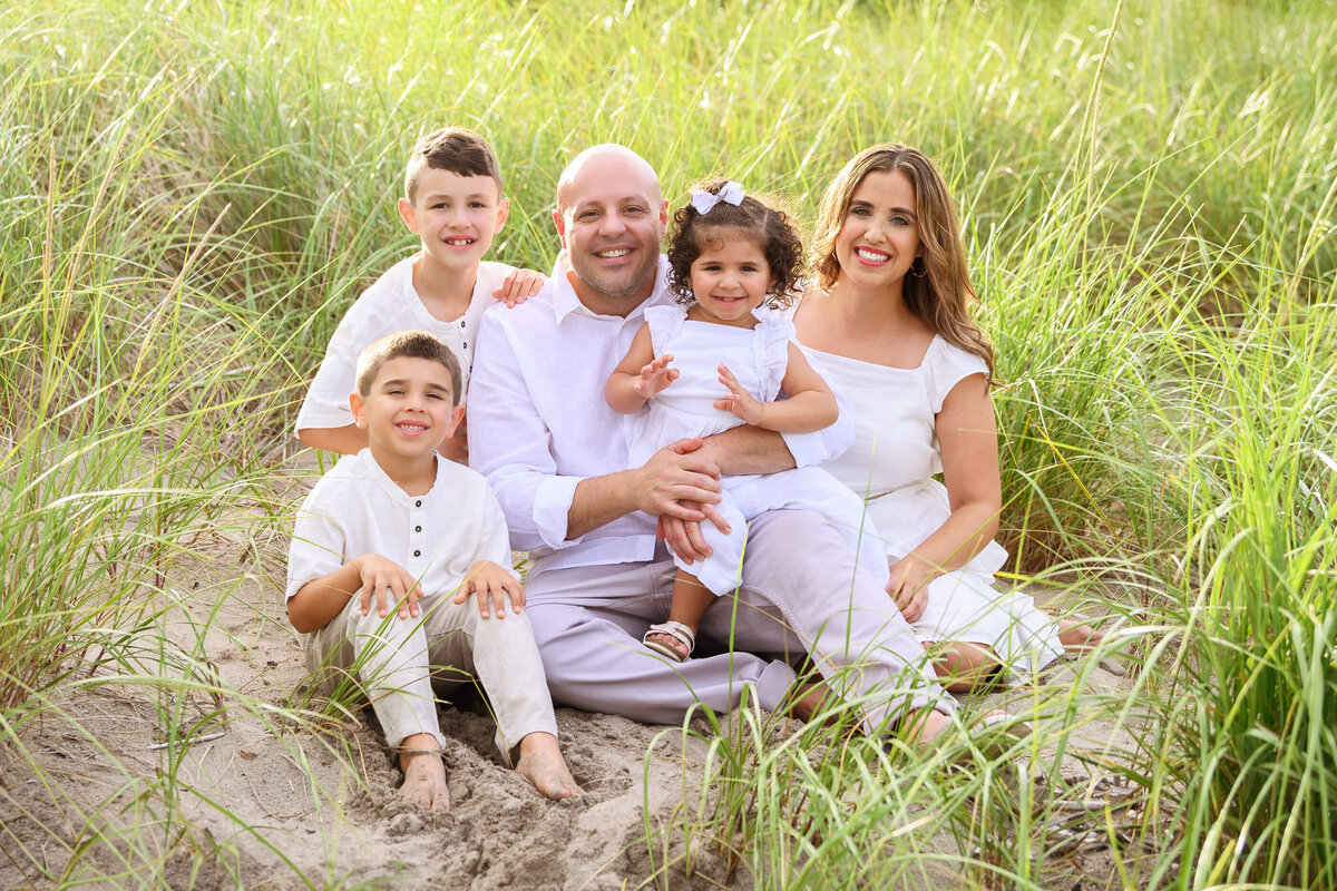 mom and dad sitting in the sand with their three children for their Burlington Beach family photos