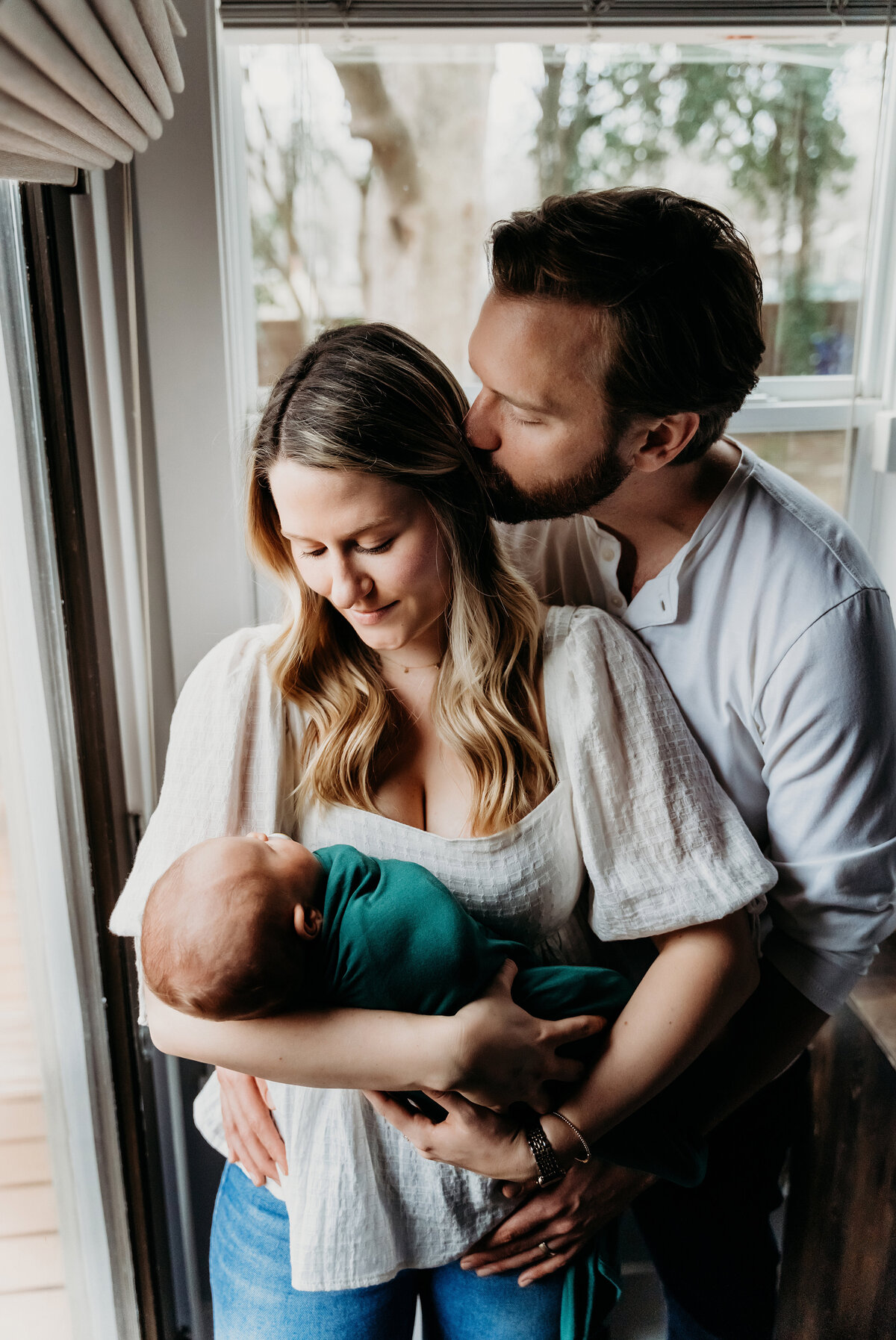 Newborn Photography, a mother holds her baby at home, husband kisses mom