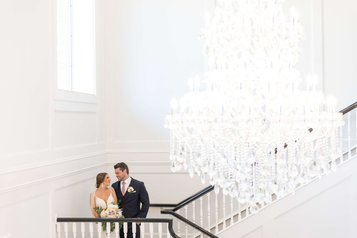 Bride and groom on the staircase in front of chandalier at wedding at Stones River Country Club