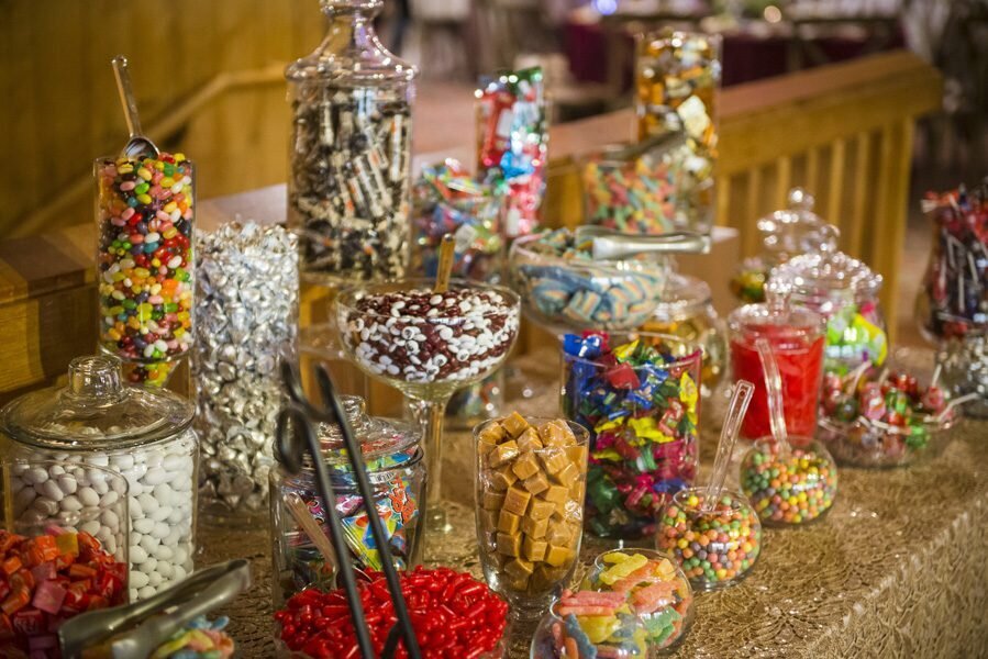 A candy bar at a wedding features a dozen various shaped glass containers of colorful candies.