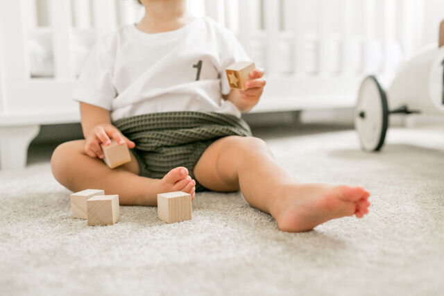 A baby on his first birthday sitting on the floor playing with building blocks in Surrey