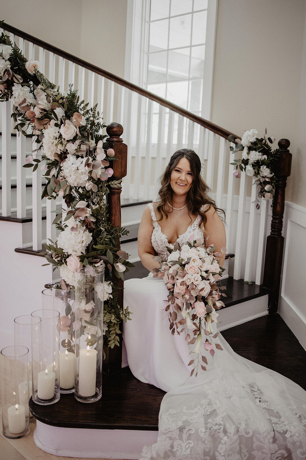 Beautiful bride in a white wedding dress sitting on a staircase with flowers, showcasing radiant skin and wedding day makeup by Skinlux Beauty Bar.