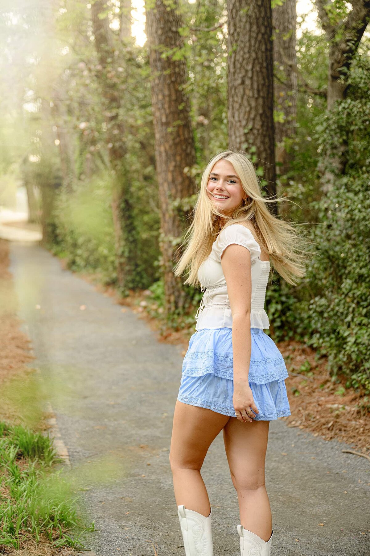 blonde charlotte area senior laughs as her hair blows around her during her senior photos wearing a white top, blue skirt, and white boots