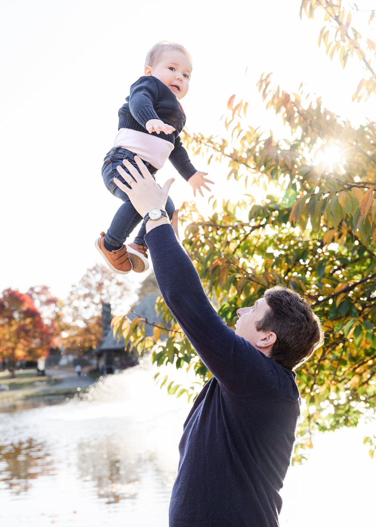 Lifestyle photo of mother throwing smiling son at an Essex County, New Jersey park in the fall.