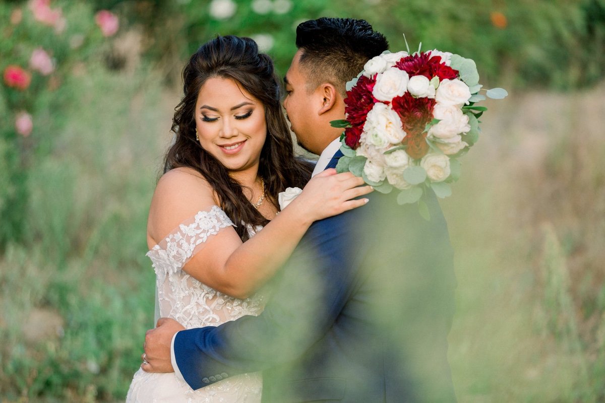 Groom whispers into his Bride's ear as they embrace during a moment alone in a field