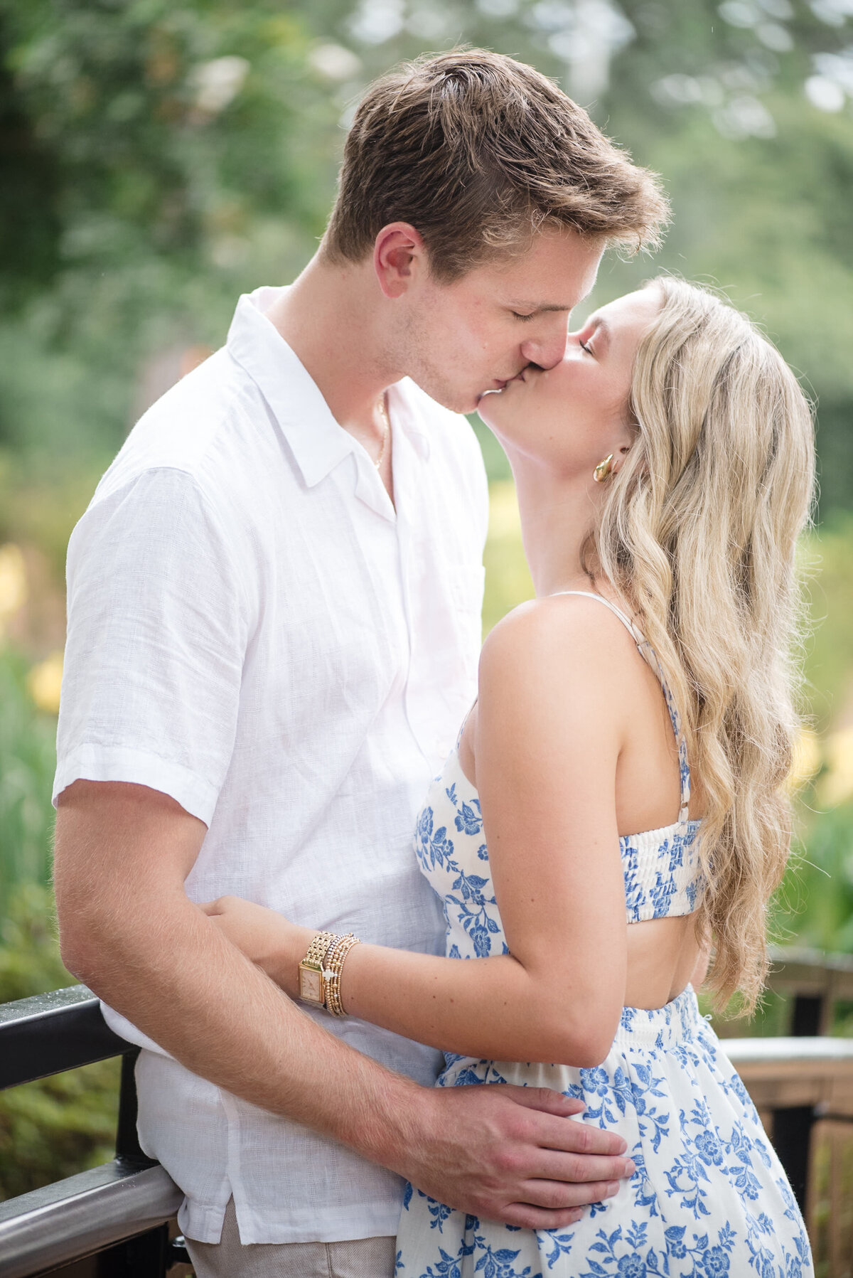 Engaged couple kissing on the bridge in the WRAL Azalea Garden surrounded by greenery in Raleigh, NC—captured by DeLong Photography, a top Raleigh wedding photographer highlighting the most romantic and natural photo locations in the Triangle.
