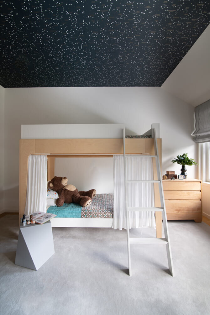 Interior decorators in Boston, MA, design a boys' bedroom with navy blue ceiling wallpaper, natural wood bunk beds, and a side dresser for a modern, cozy space.