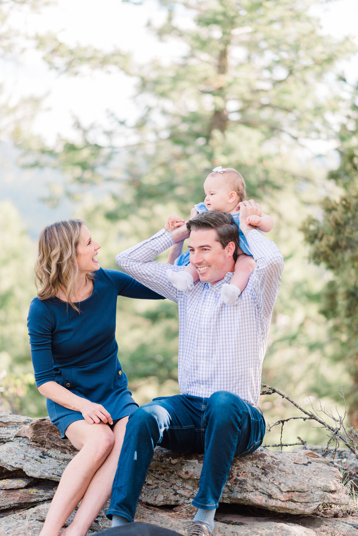 denver family photographers photographs young famil yin the woods of the Rockies sitting together on a log playing with their baby for their family outdoor photos