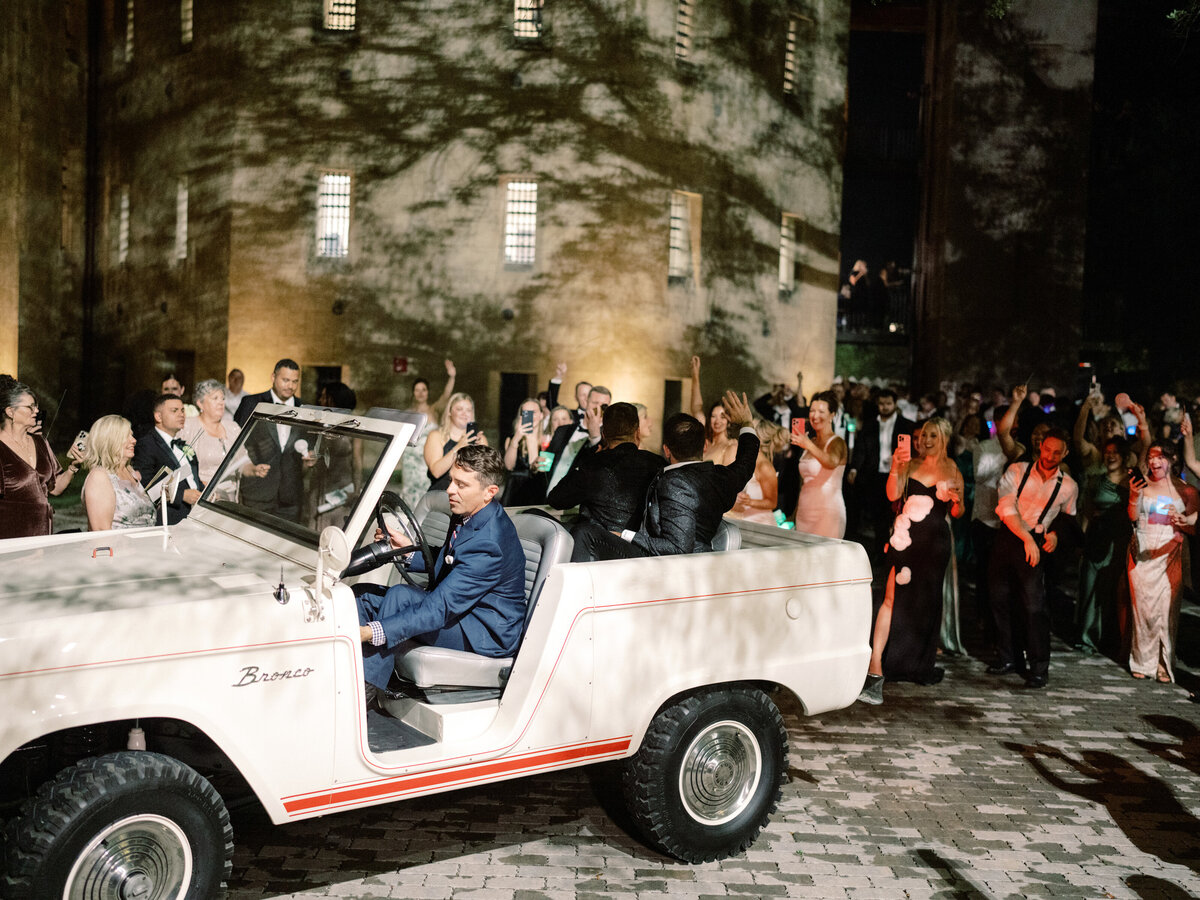 A couple drives away in a classic vehicle after their celebration, embodying joy and excitement from their unforgettable night surrounded by loved ones.