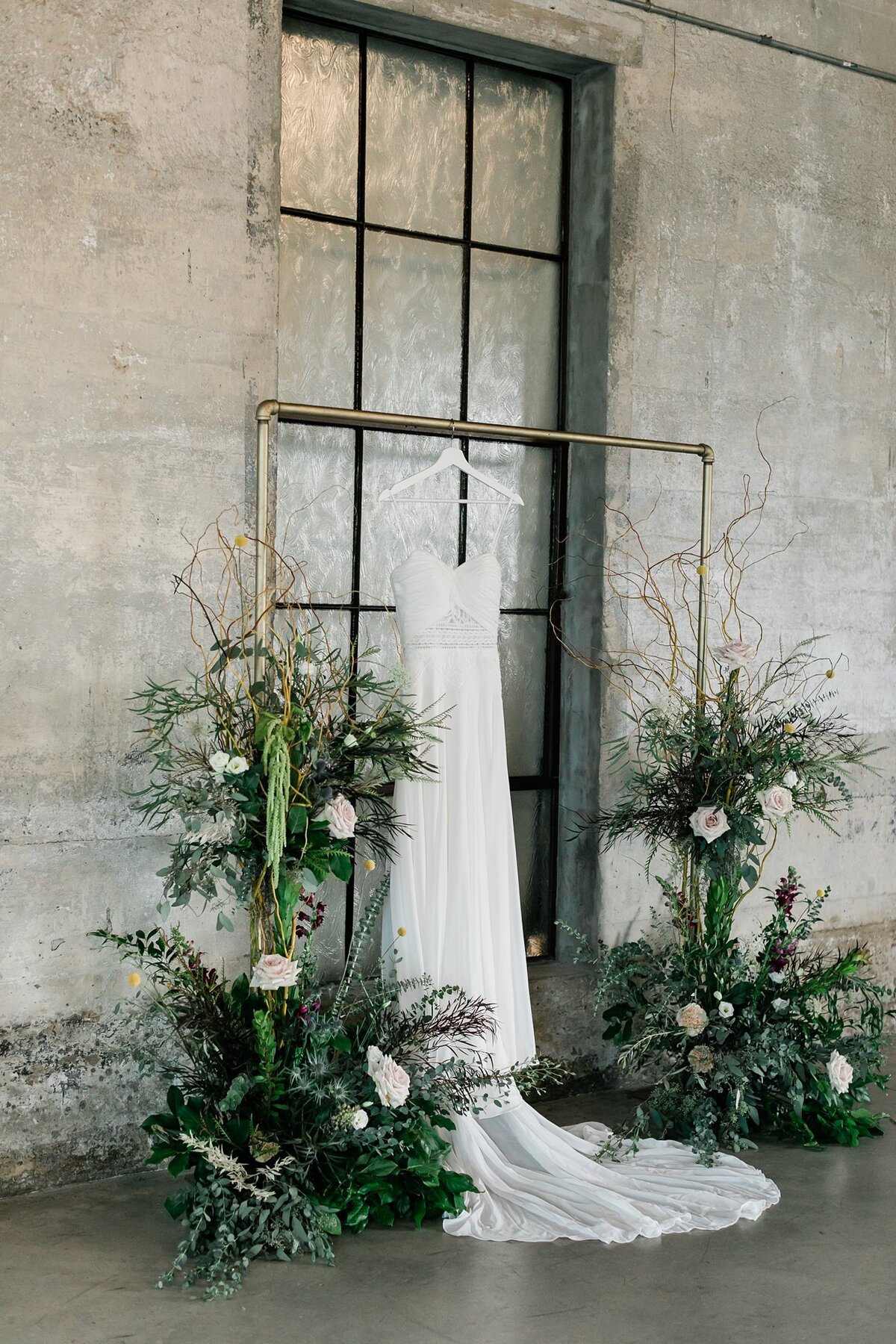 Bride's boho wedding dress hanging from her arch in the chapel at Olde Dobbin Station surrounded by greenery and florals.