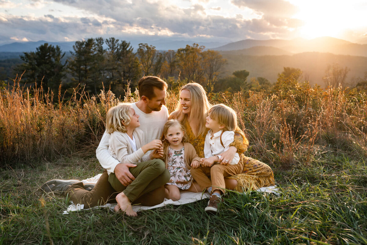 A mom, dad and their children hug and laugh on a mountain top near Asheville NC