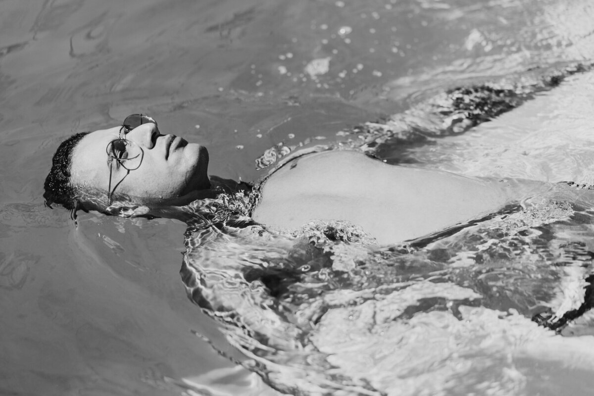 Black and white underwater editorial image with model floating in still water, evoking calm and cinematic mood.
