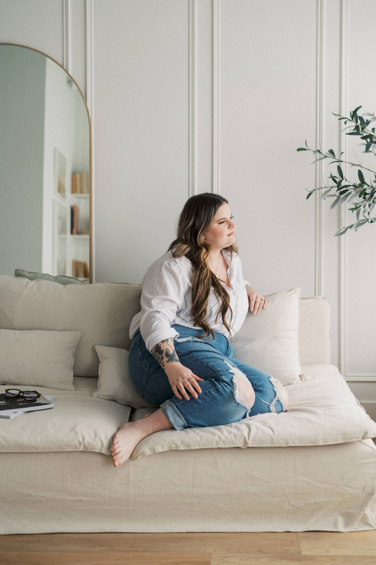 Brand photo of woman sitting on white couch wearing white shirt and blue jeans