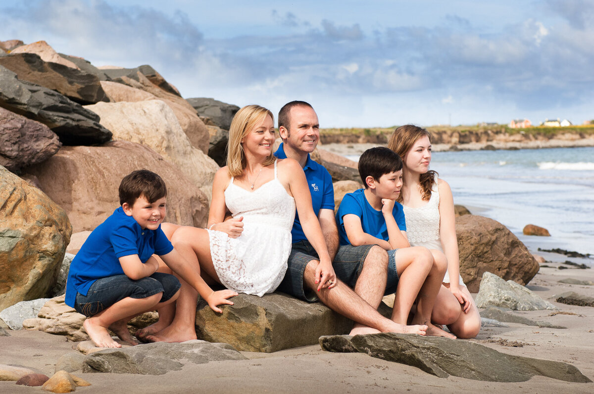 portrait of a family of five wearing summer clothes, sitting on rocks on the beach