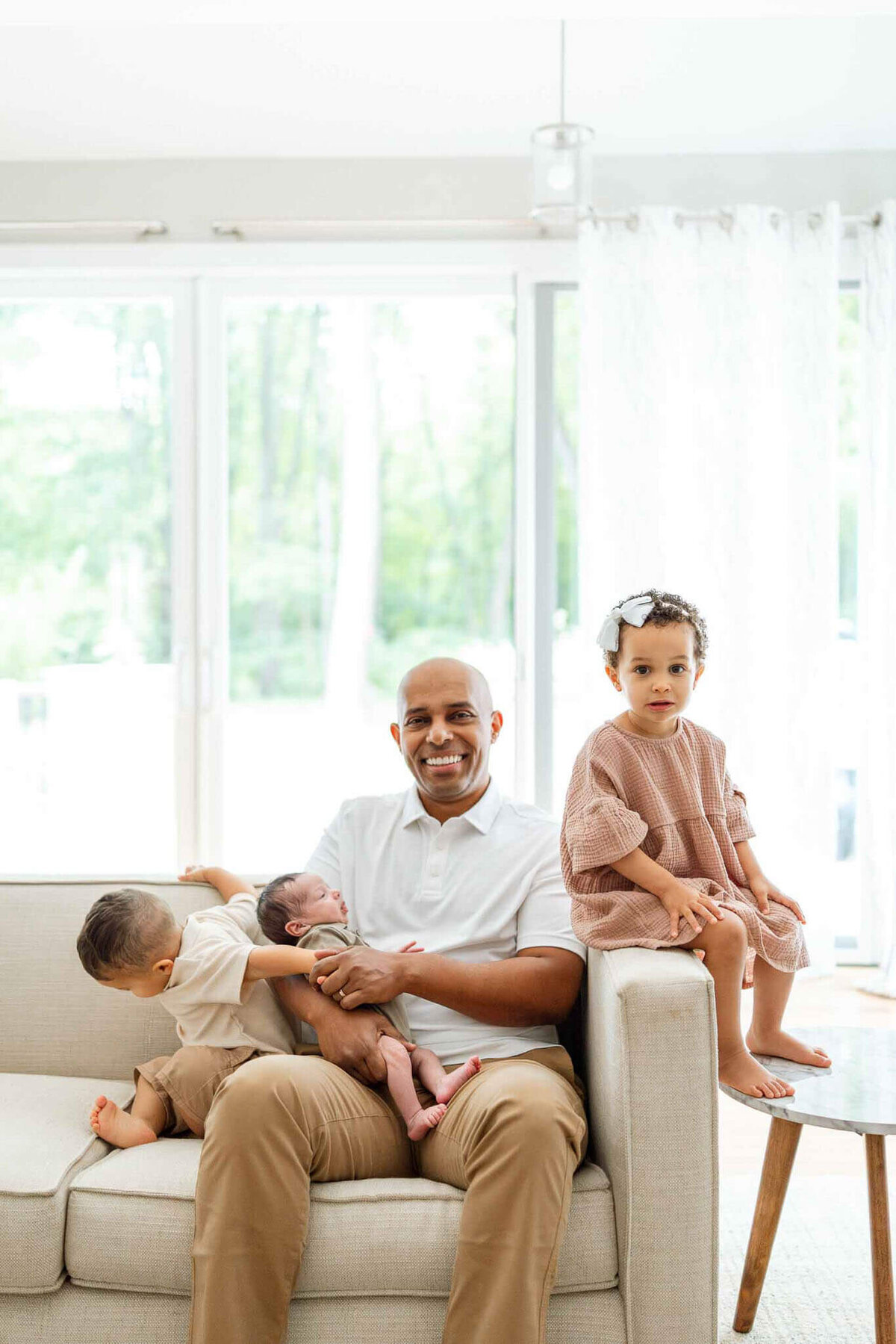 A proud dad holding newborn while older son and daughter snuggles close.