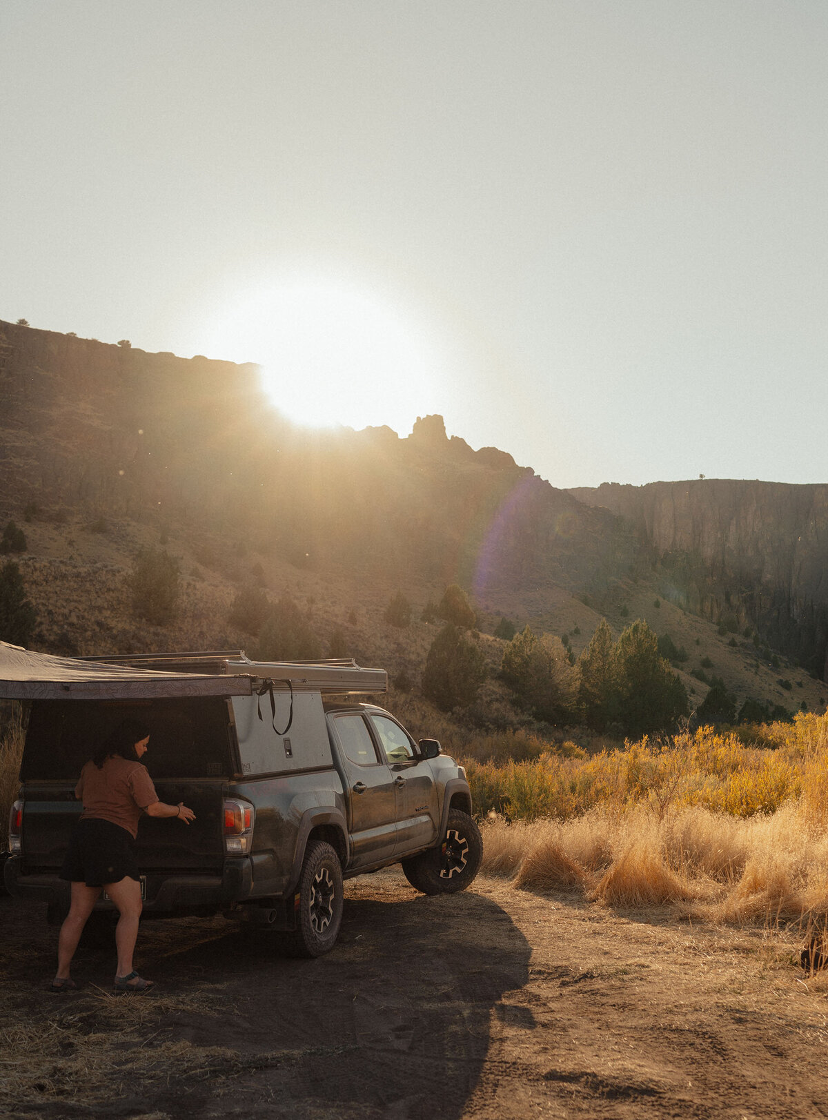 a woman stands next to her truck with a pop up camper in the golden sun in Moab, Utah