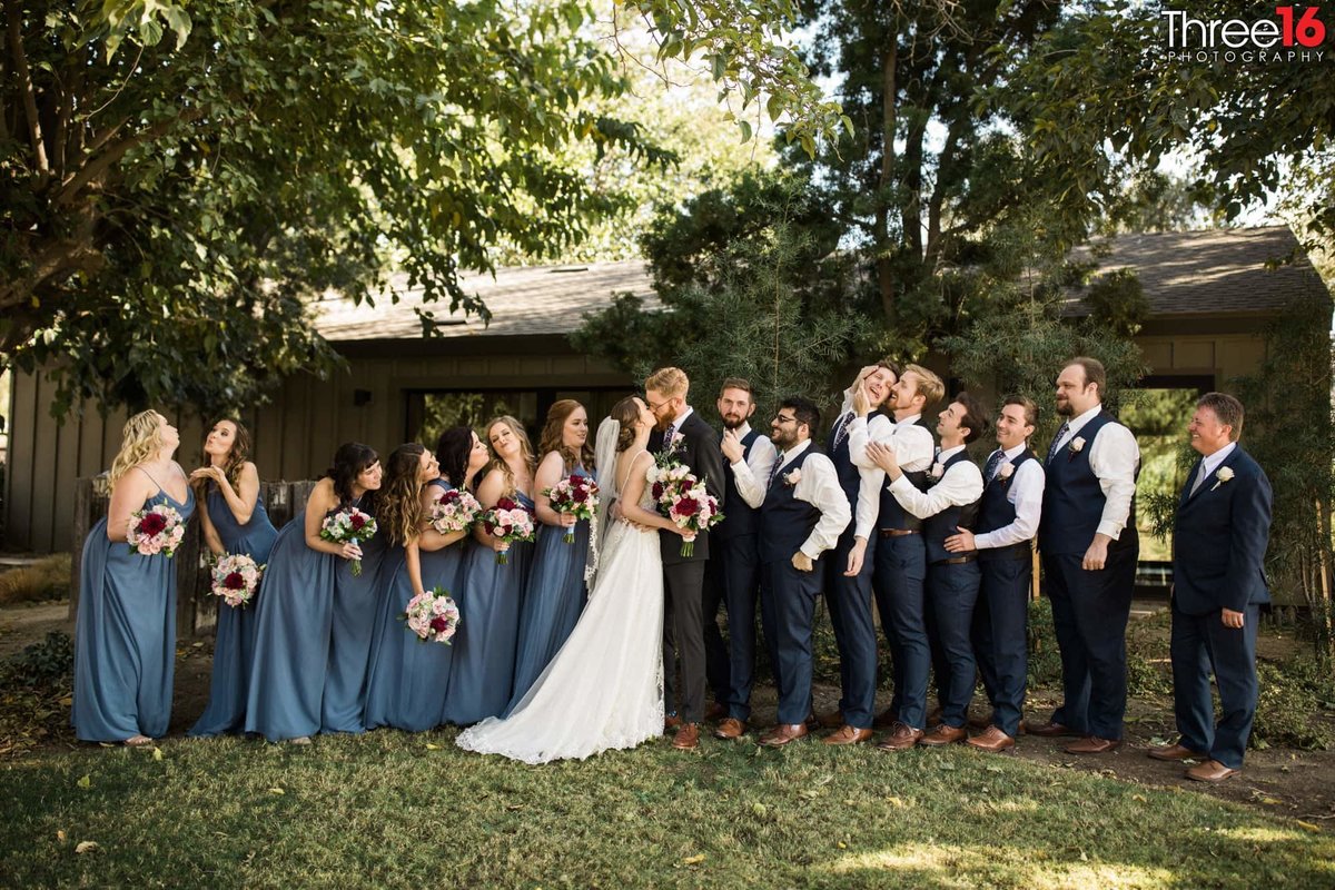 Couple kisses while wedding party goofs off