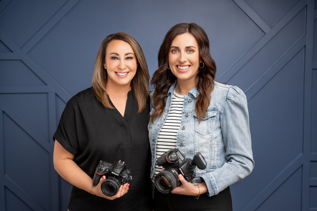 Two women photographers posing together with their cameras and similing