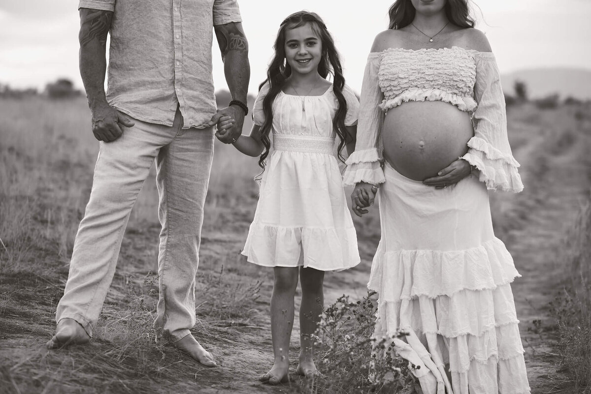 A young family poses fot this bkack and white portrait. Focus is on the young daughrer in the middle looking at the camera and smilling Taken by Brittany Danielle Photography in Valleyview Nature Park