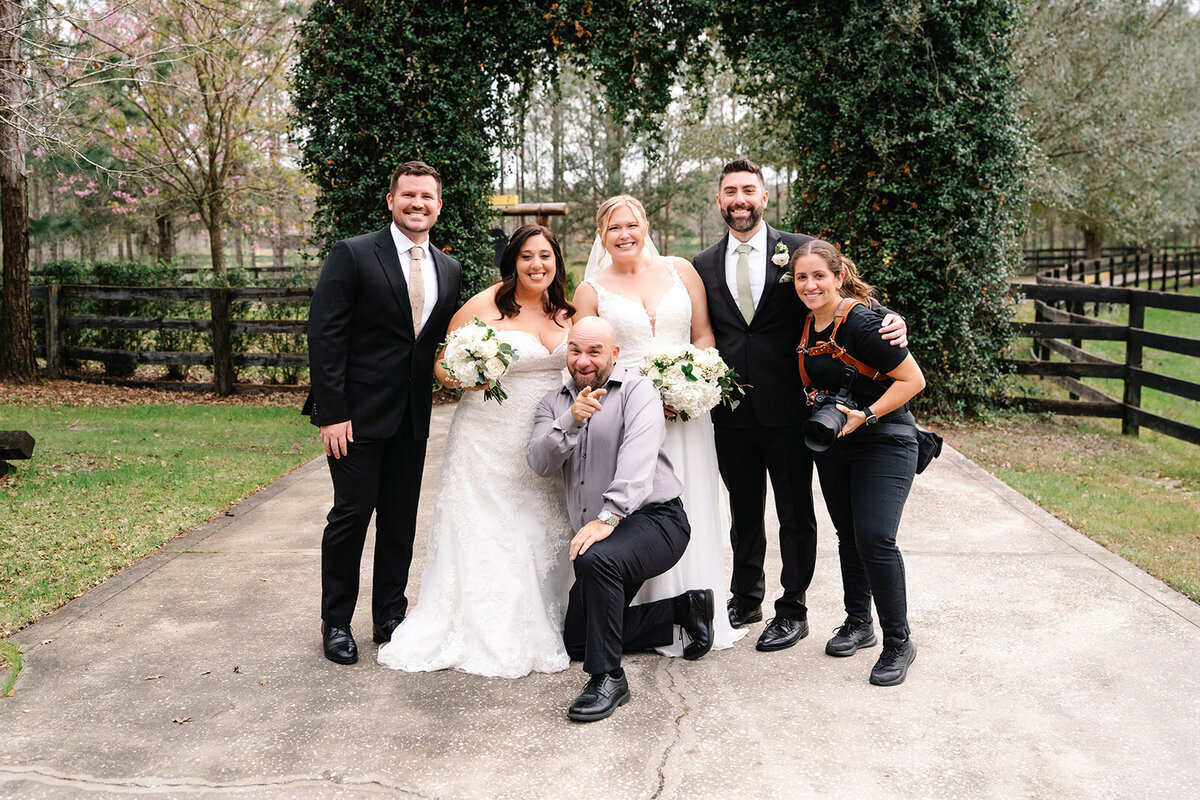 Female Queer wedding photographer posing with two brides and friends from the LGBTQ+ community at Club Lake in Apopka, Florida, after their ceremony.