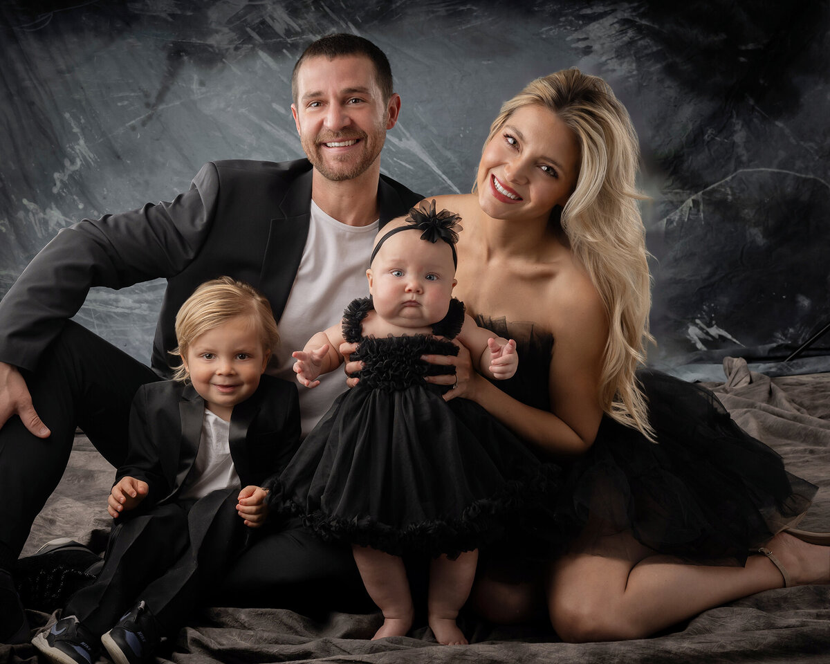 Family of 4 sit together and smile in their Iowa Family Photographer’s Studio