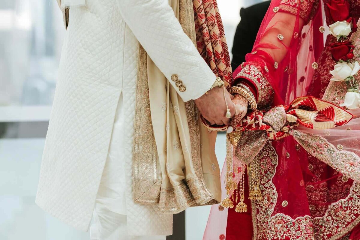 South Asian bride and groom holding hands in as they walk around the fire.