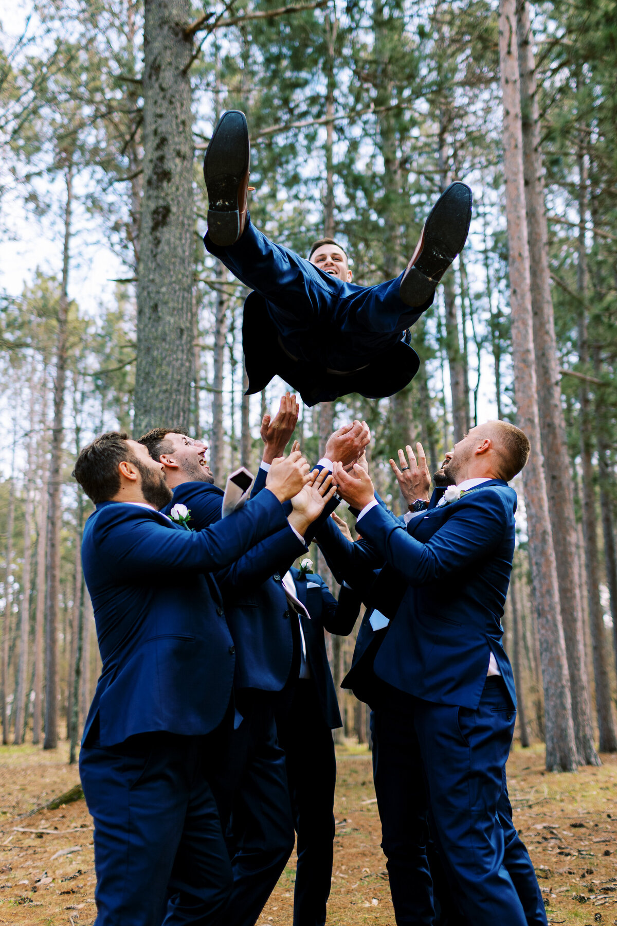 Groomsmen tossing groom into the air with joy