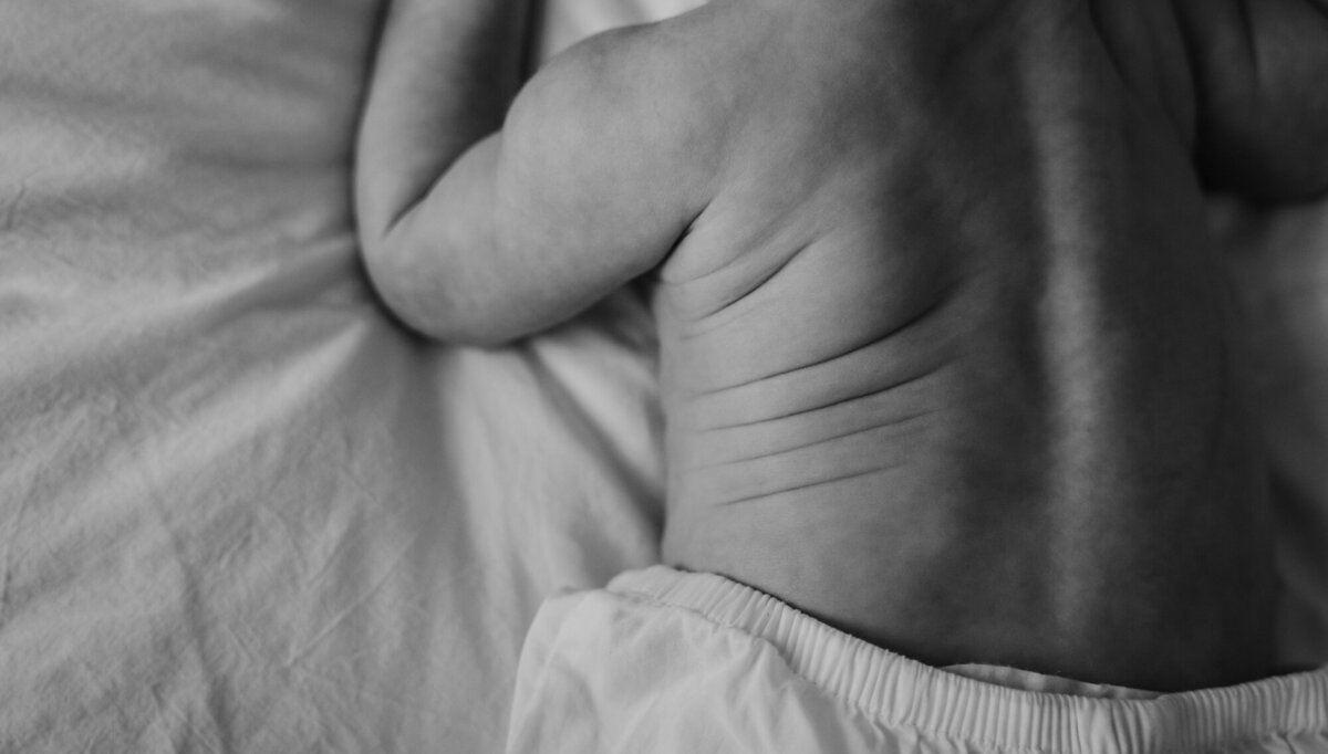 Newborn Photography, Baby's back rolls while baby is face down on the bed, in black and white.