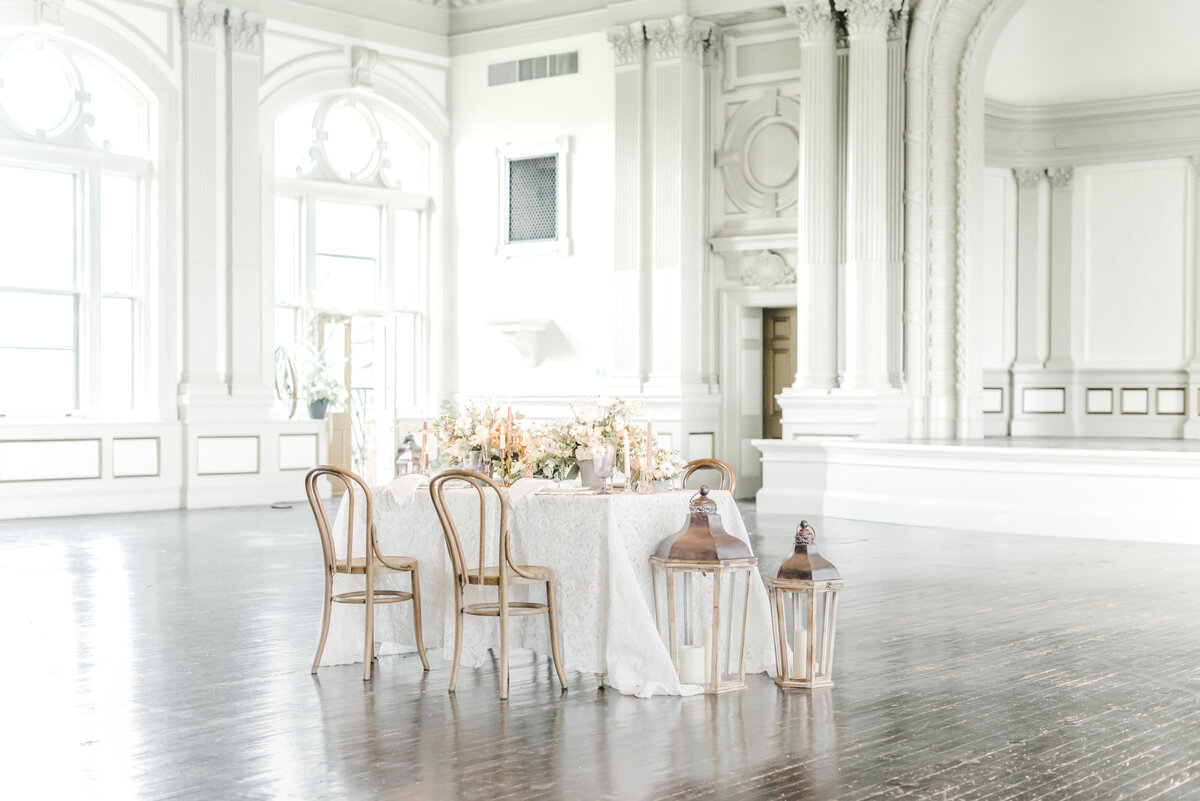 intimate wedding reception in a Bright and airy ballroom centered by a  table with peach and ivory flowers