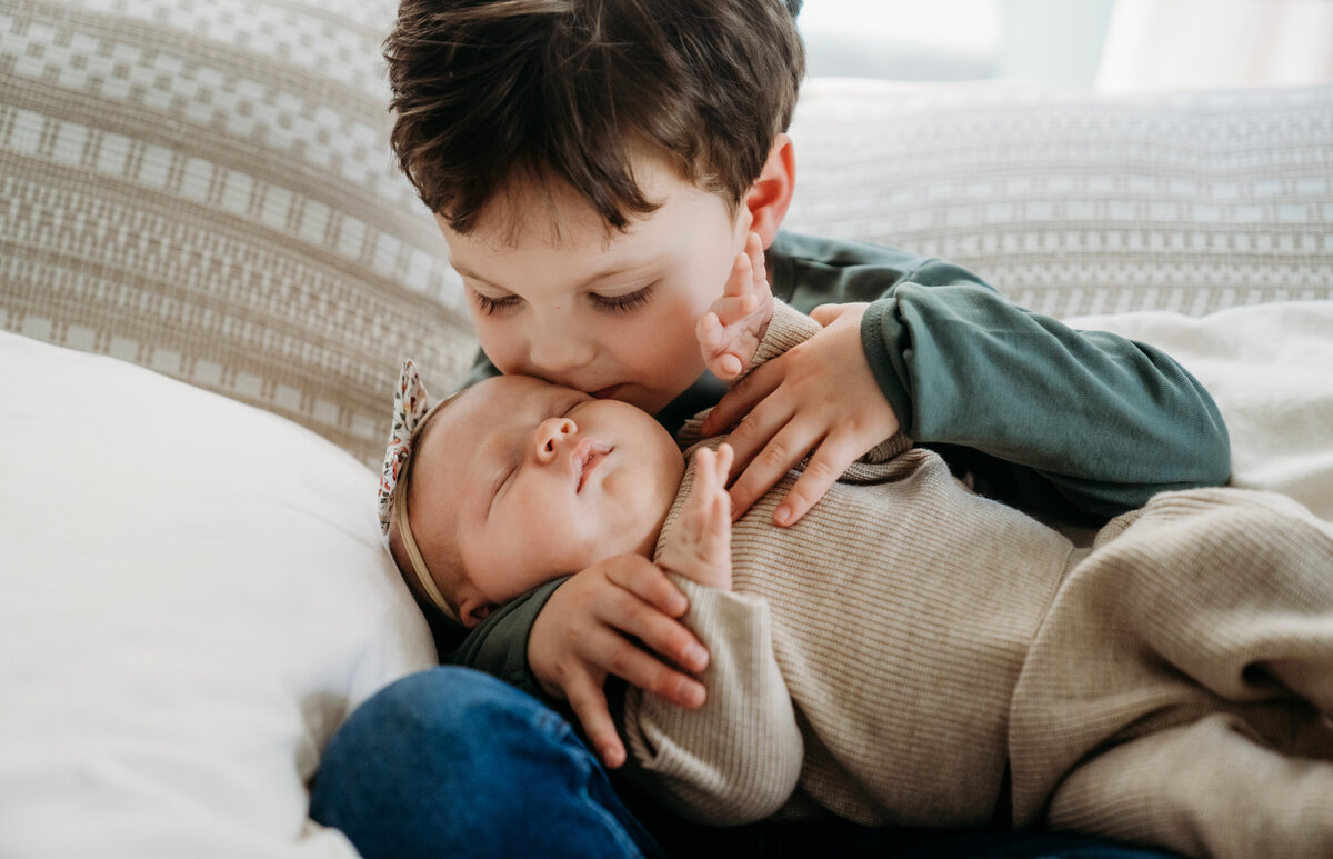 Newborn Photographer, an older brother holds his baby sister and gives her a kiss