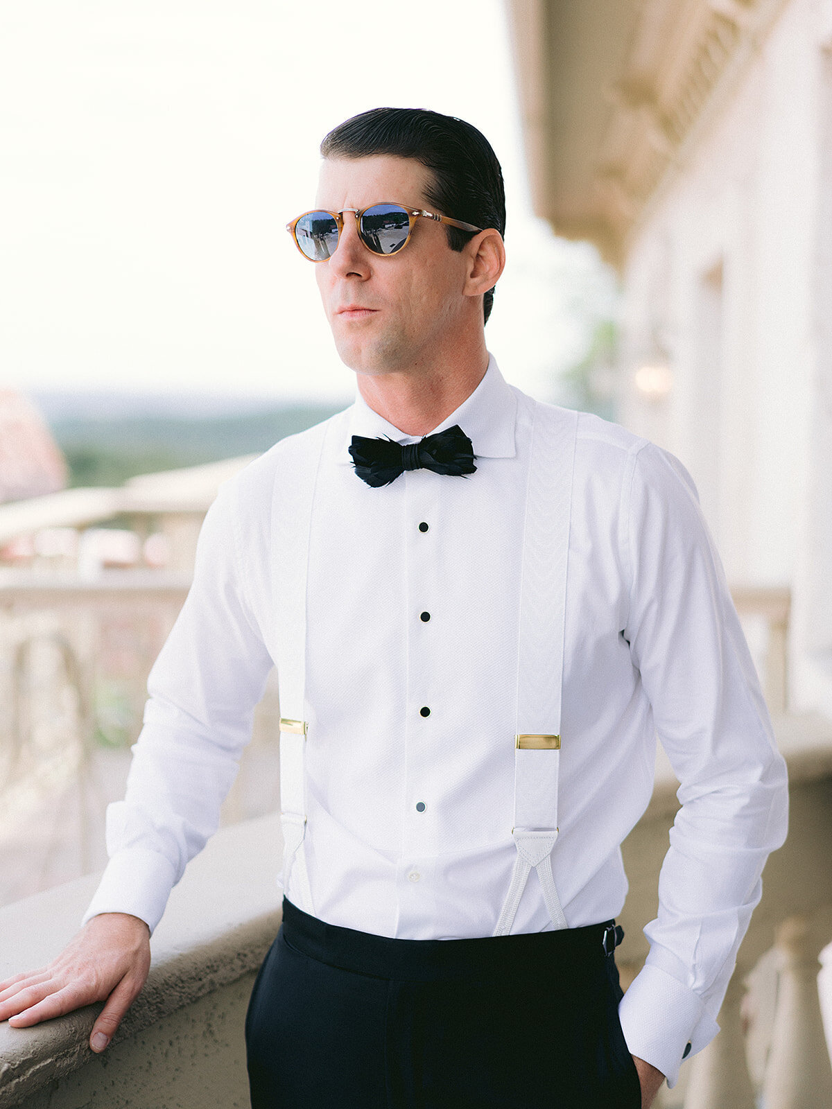 The groom poses on the balcony of the groom's suite at Villa Antonia, wearing sunglasses