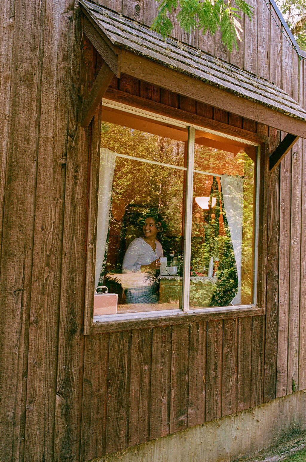 A bride smiles through the window of a wooden building.