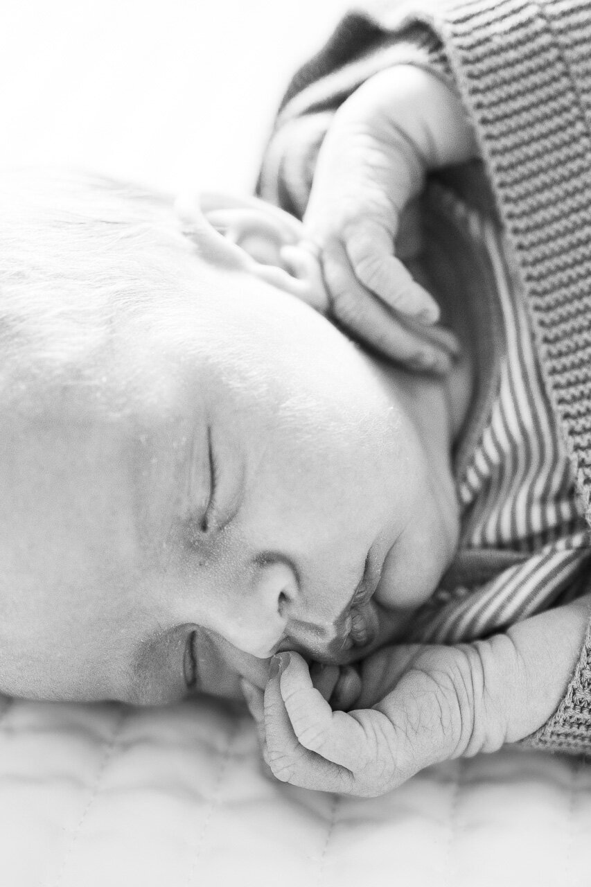 Beautiful black and white image of newborn baby's face with hands curled near his nose and ear by lifestyle newborn photographer in Tifton Georgia