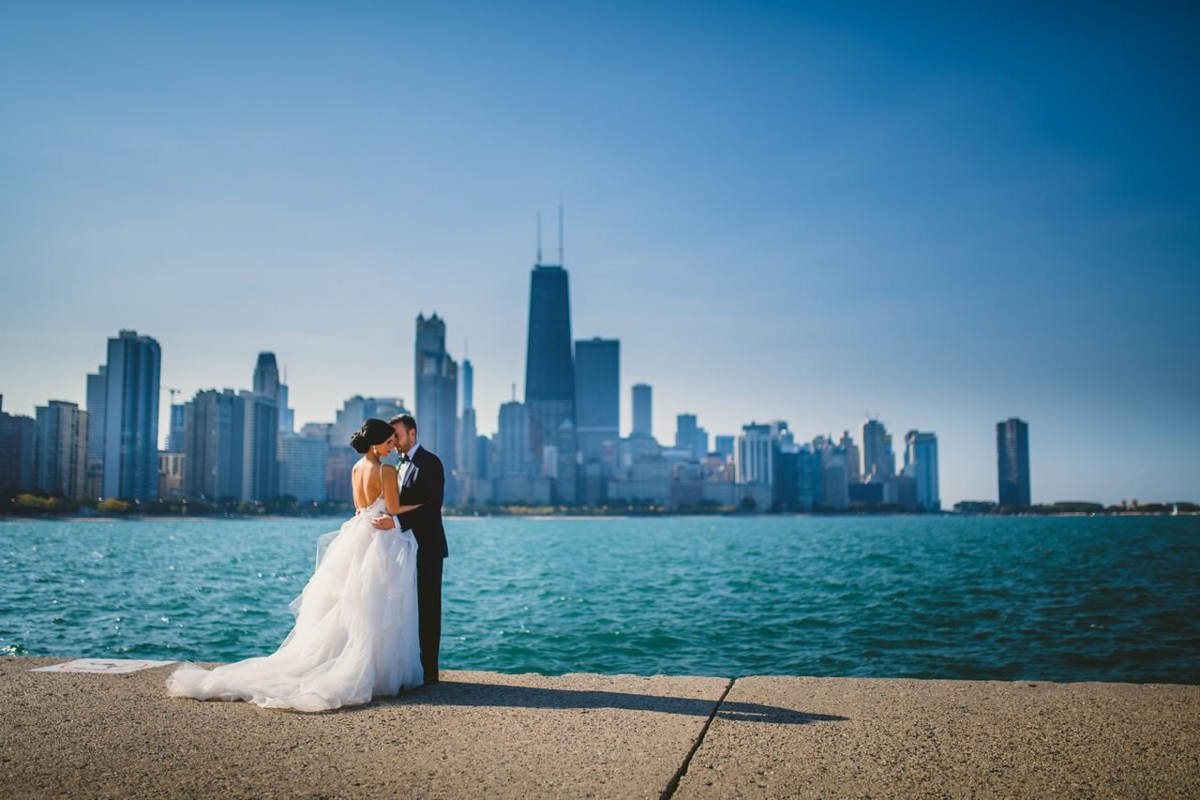 Bride and groom embrace along the water with the Chicago city skyline in the background