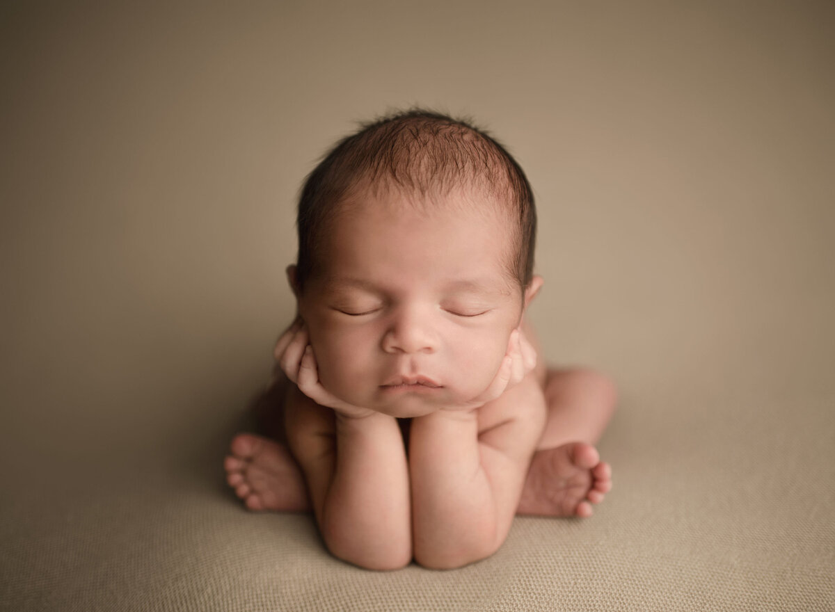 Newborn baby boy is posed for his Murrieta newborn photoshoot. Baby boy is bare and sitting in a froggy pose with his hands propping up his chin. Captured by best Murrieta newborn photographer Bonny Lynn Photography