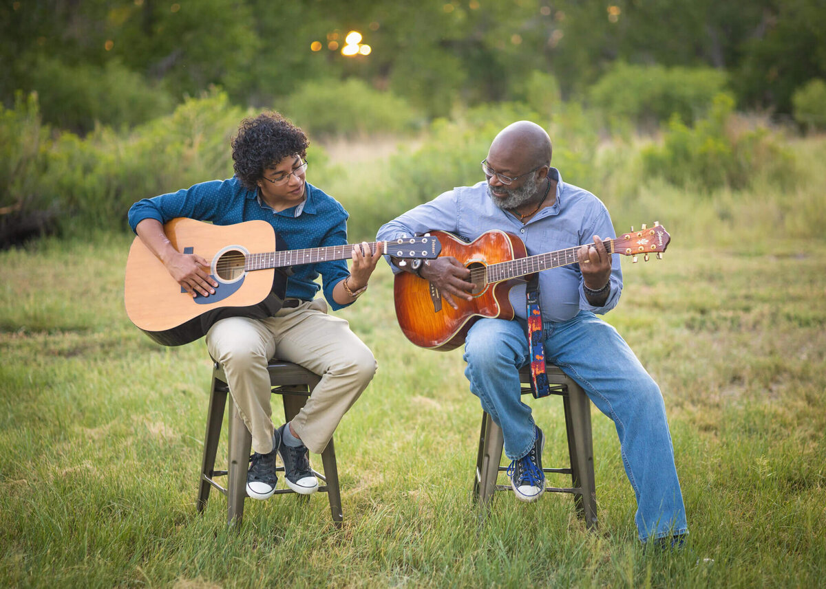 a father and son sitting in a field playing guitars