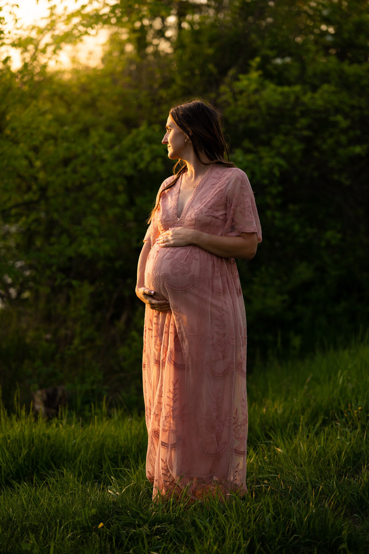 Woman holding her pregnant belly in a pink Pink blush Maternity Dress.