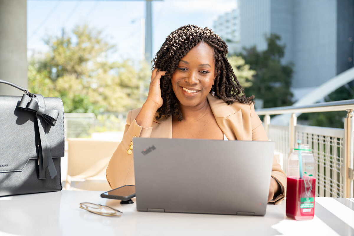 A woman working on a coffee shop looking a her laptop and drinking a juice