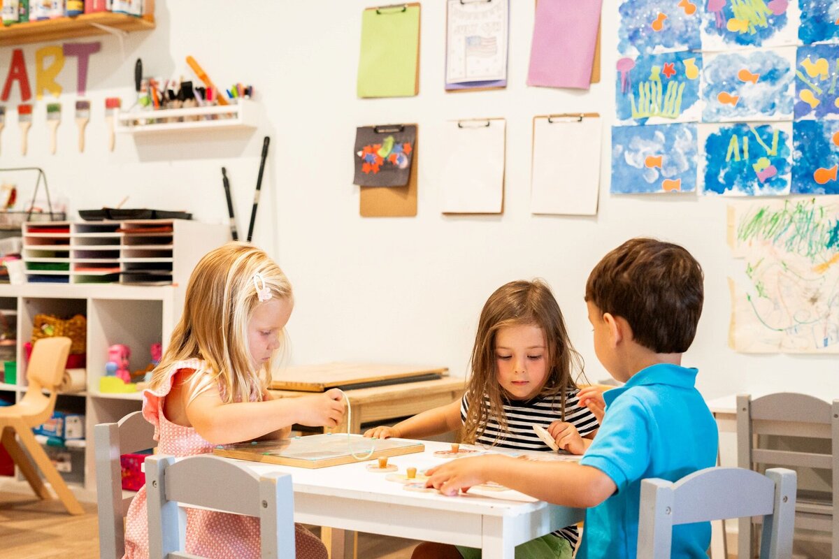 Three toddlers sitting at a table playing with puzzles Tree branches at the Nest, a natural learning center in Surf City, NC