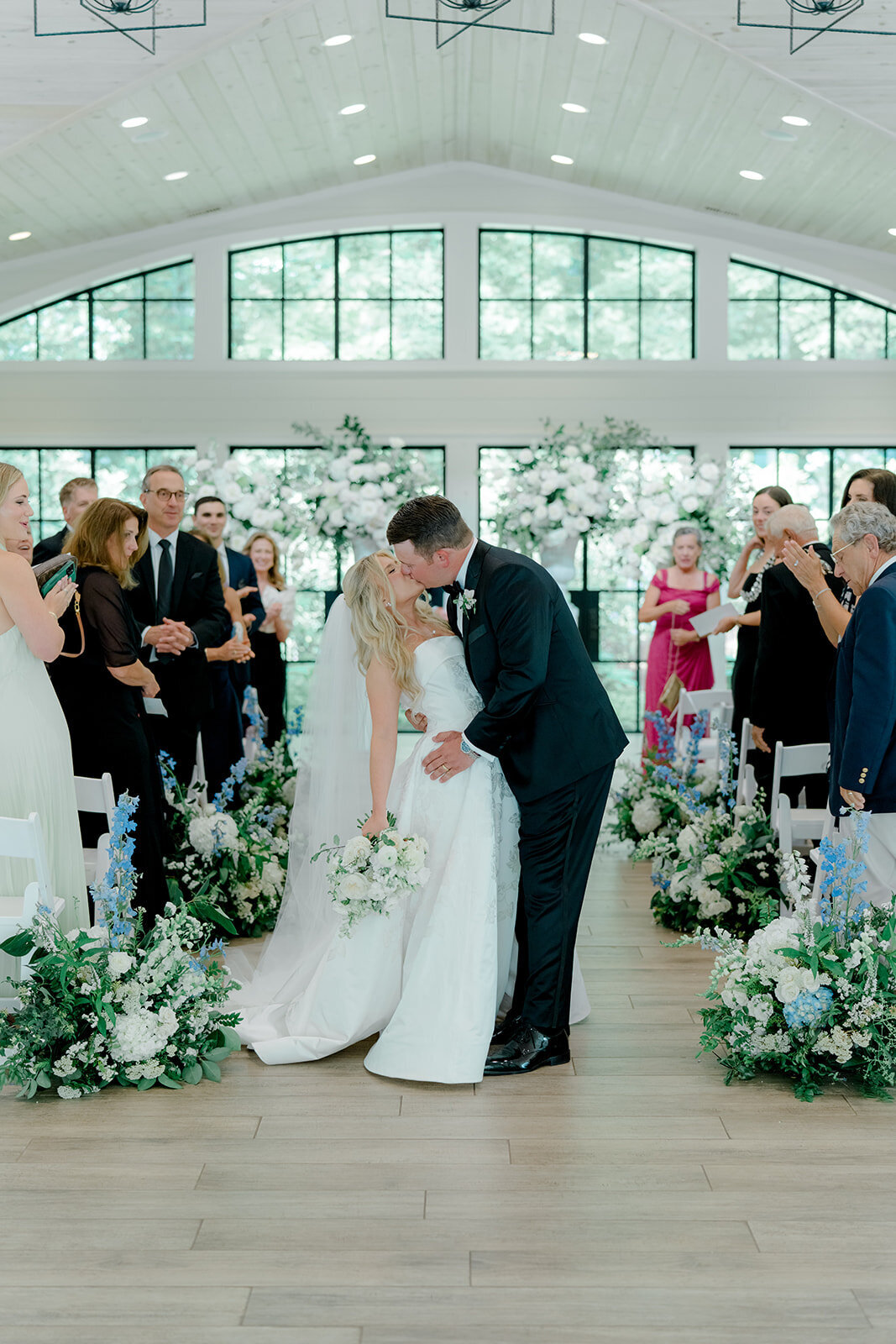 Bride and groom kiss during ceremony recessional surrounded by white and blue florals.