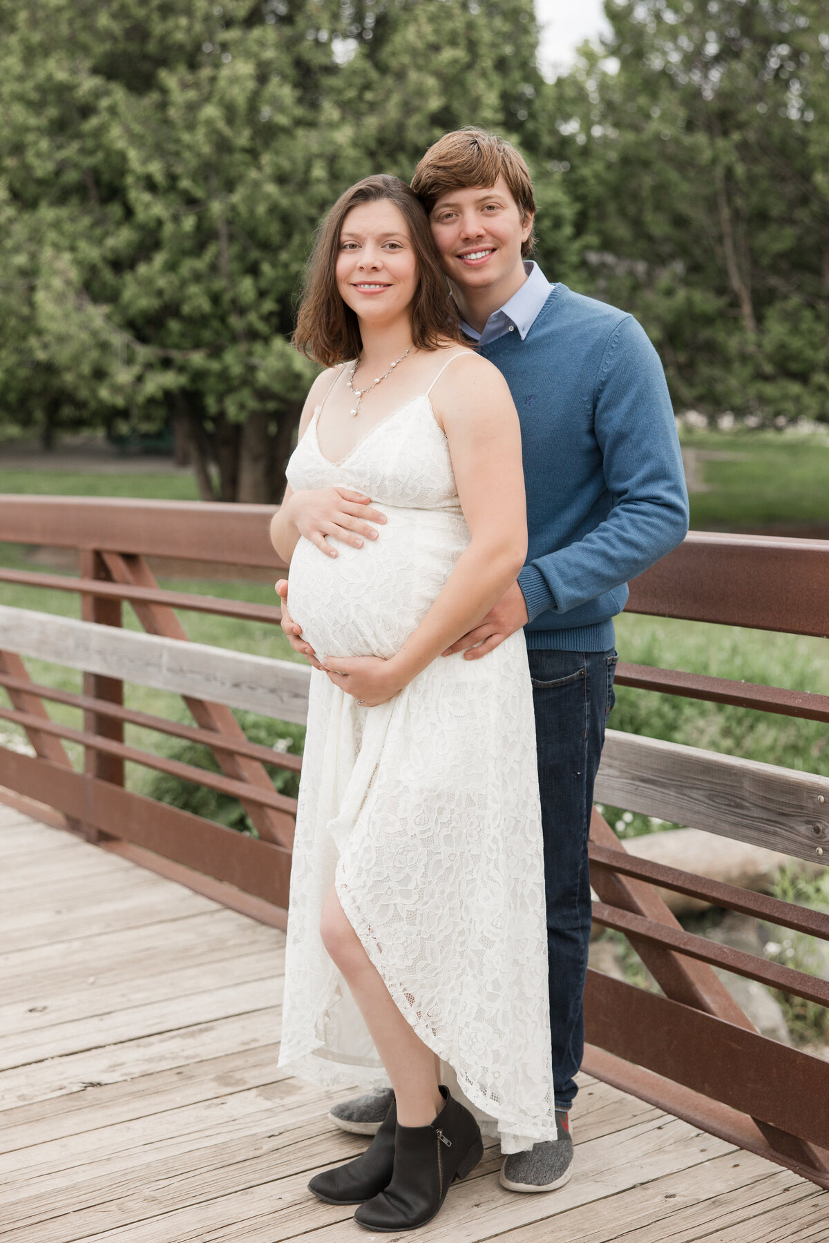 Expecting couple holding each other on a bridge and smiling at the camera