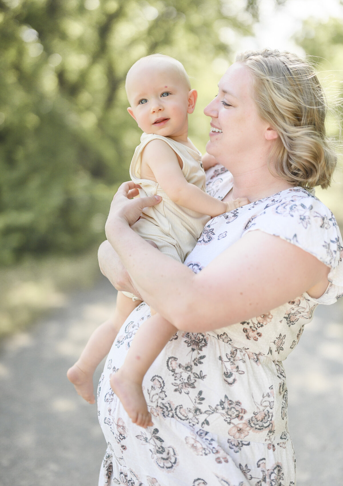Mother lovingly holding her baby boy close to her shoulder in a warm, sunlit outdoor setting.