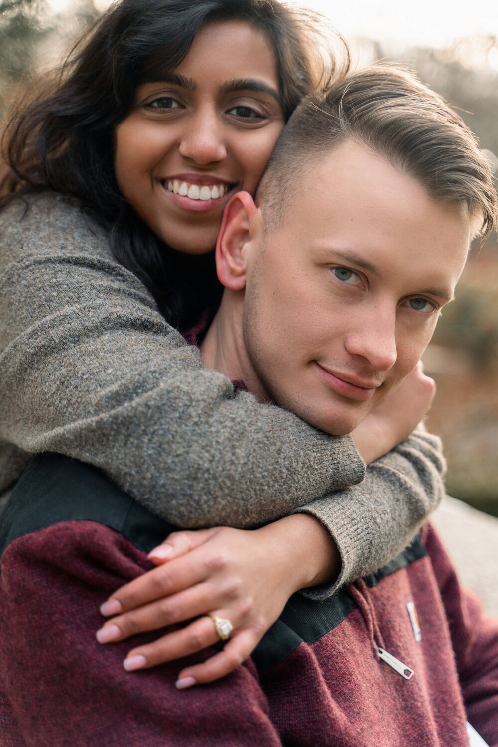 closeup of Indian woman embracing a White man from behind while both smile at the camera