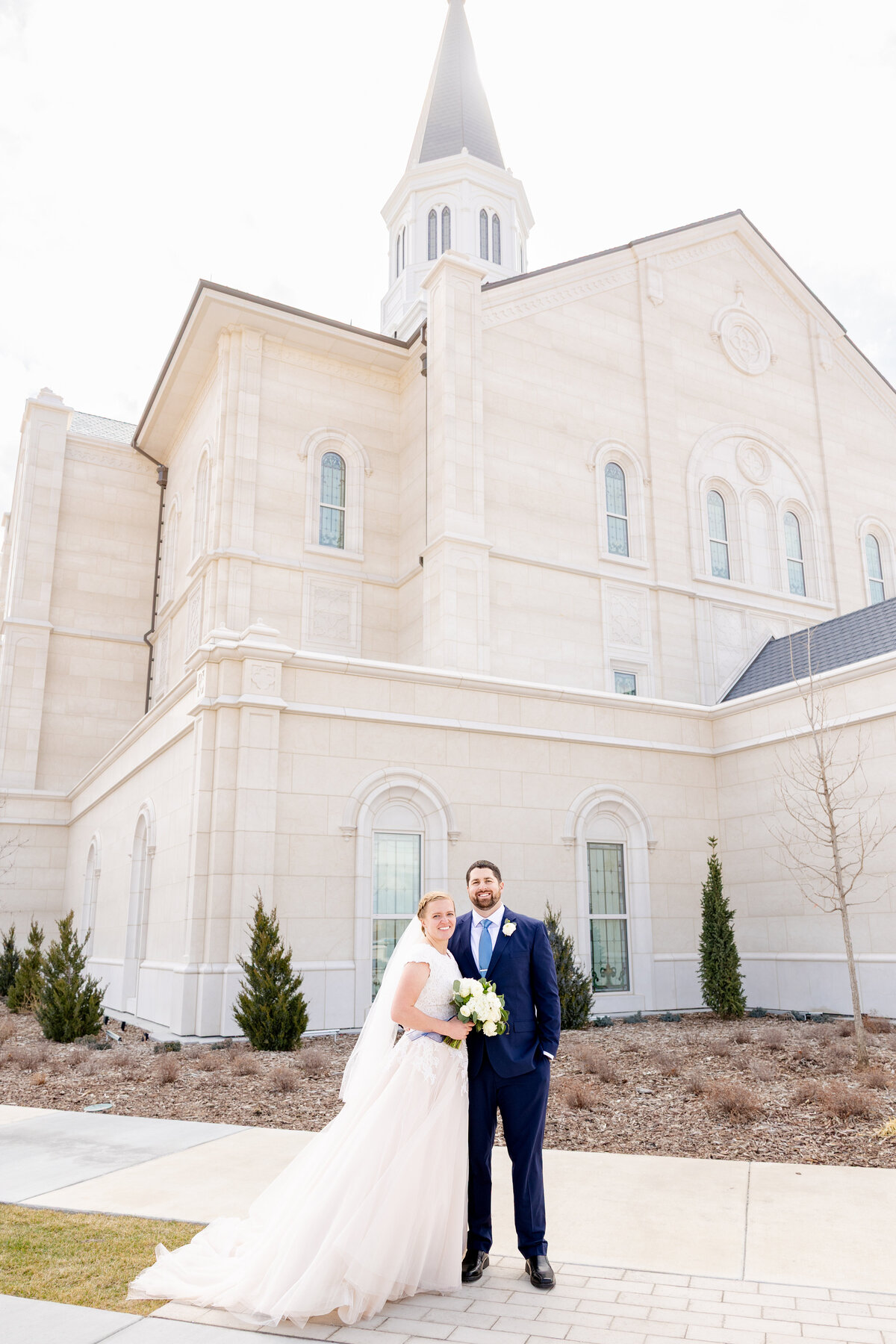 The newlyweds pose in front of the LDS temple, smiling as they stand arm in arm with the temple tower in the background.