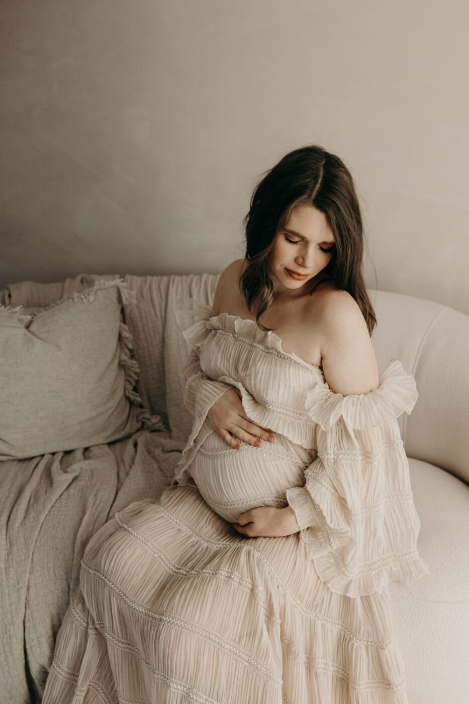 Serene maternity portrait of an expectant mother with dark hair in a soft white gown in Mullingar