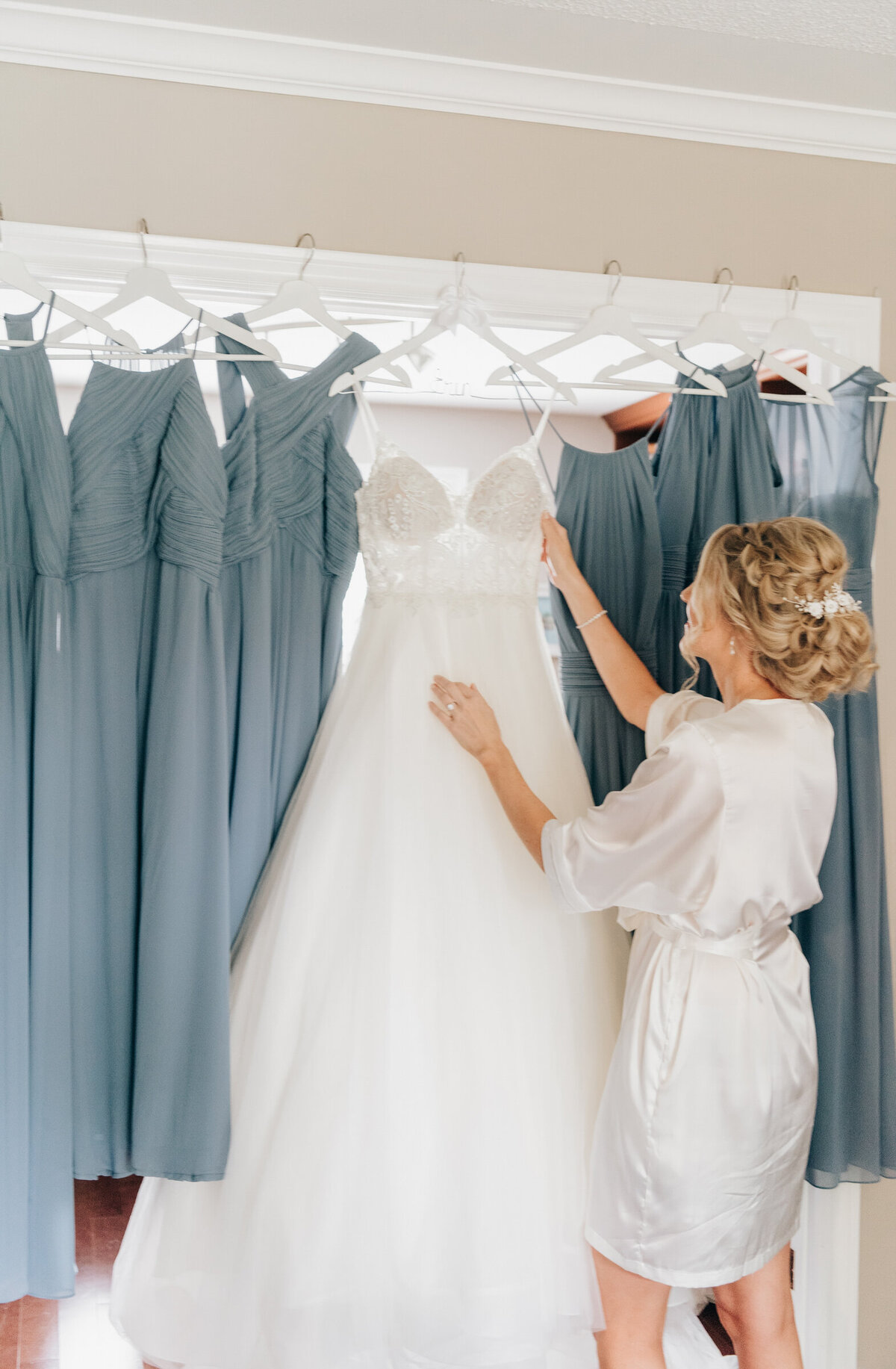 Gorgeous bride holds up her wedding dress beside light blue bridesmaids dresses while getting ready