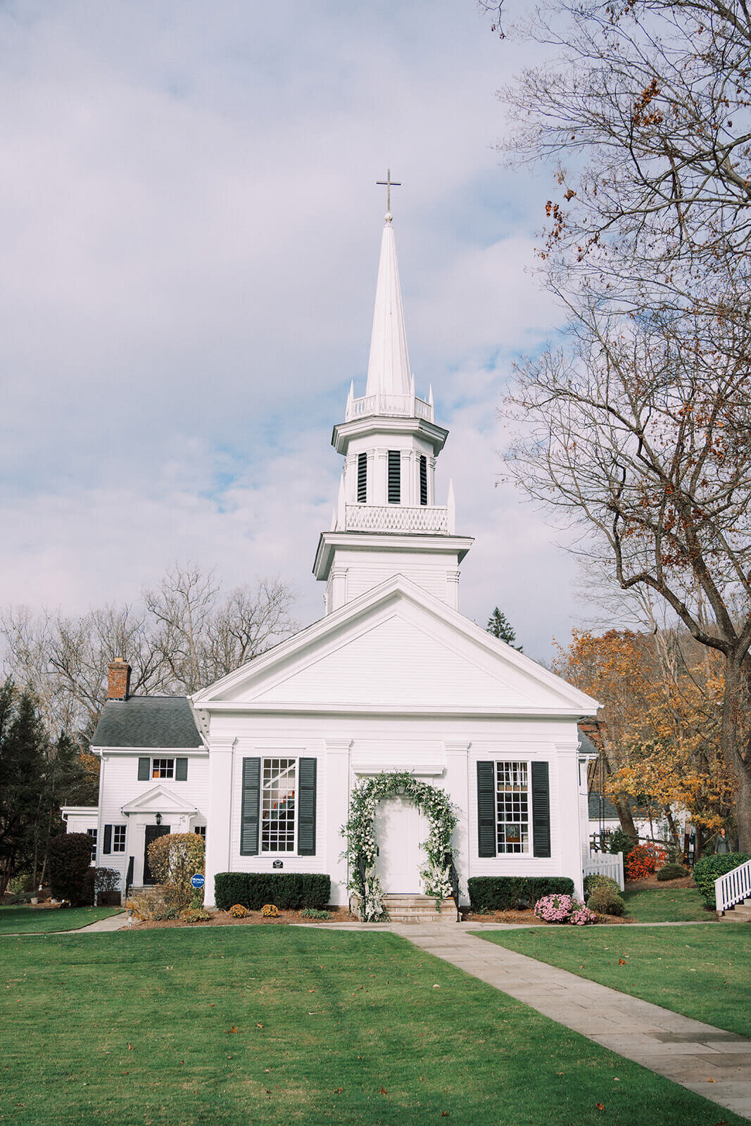 13. Classic white chapel with a tall steeple surrounded by autumn foliage.
