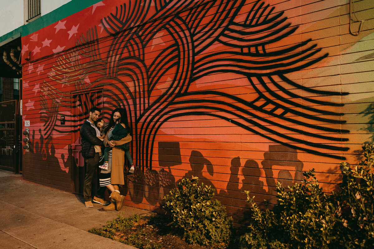 Family leans on wall with mural  of Oak tree in Jack London Square