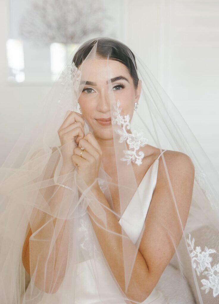 A stunning bride gently holding her lace-trimmed veil, showcasing soft, romantic details. Captured by Claudia Amalia Photography, a Florida Keys wedding photographer specializing in destination wedding photography.